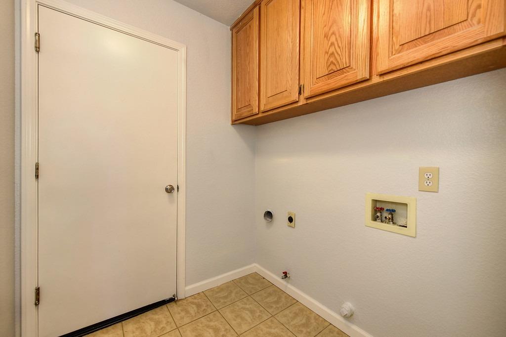 Laundry room with upper wood cabinets, tan tile flooring, and washer hookups.