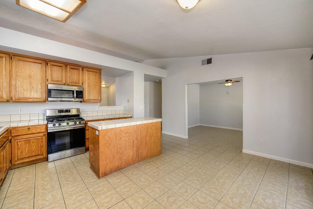 Kitchen with wood cabinets, tiled peninsula, and stainless steel appliances opening to an empty room.
