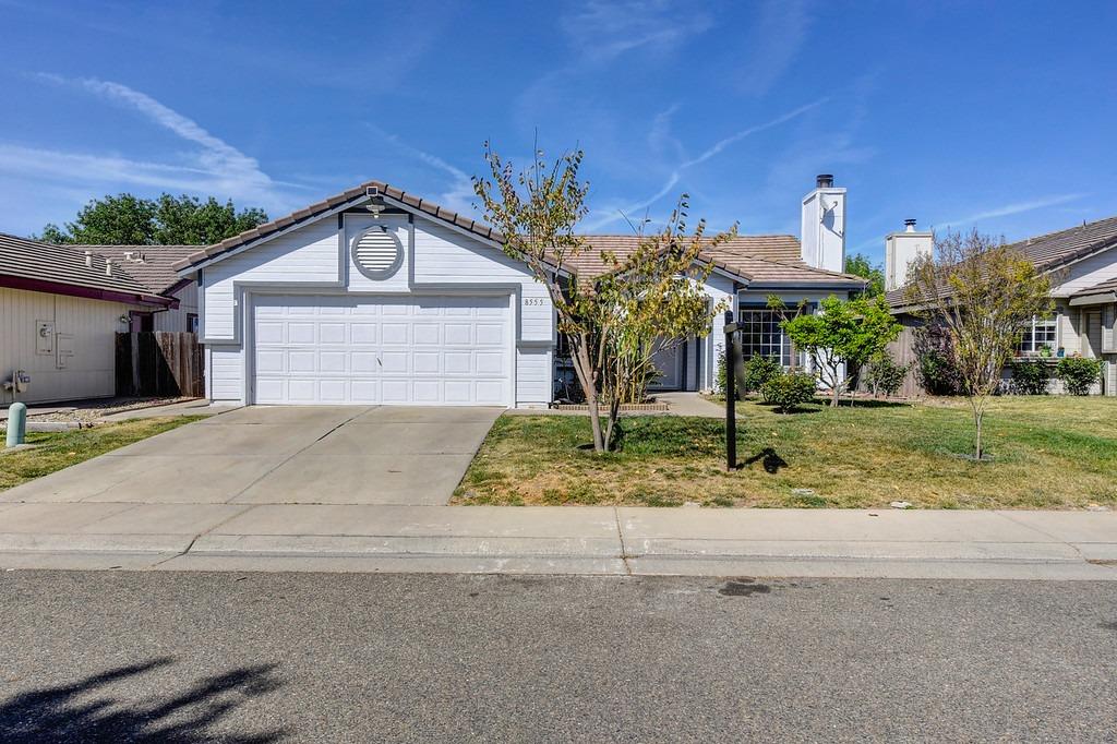 Single-story home with a white double garage door, broad driveway, and landscaped front yard.
