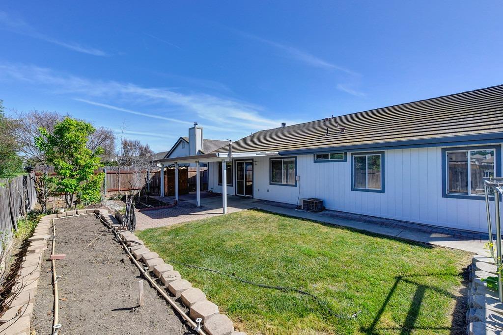 Home’s backyard with a covered patio, lawn, and raised garden bed.