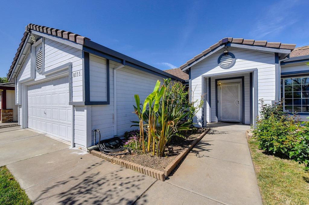 Home exterior with a two-car garage, recessed entry, and tropical plants along the walkway.