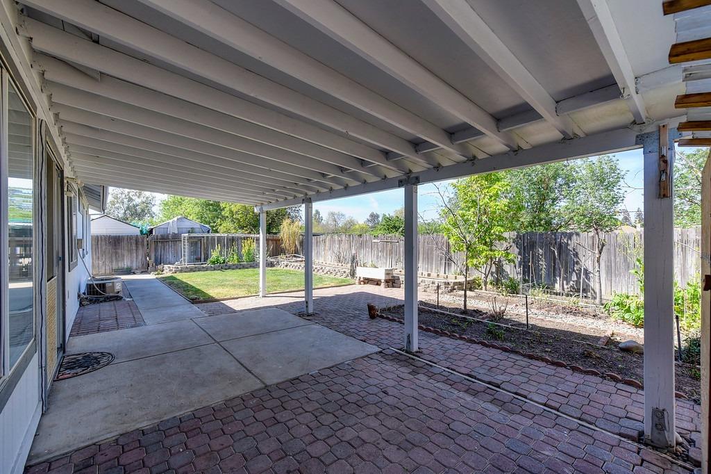 Covered backyard patio with exposed beams, brick pavers, and a fenced garden yard.