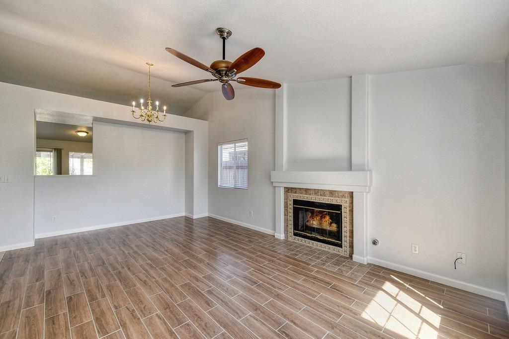 Vacant living room with a tiled fireplace, wood-look floors, ceiling fan, and adjoining dining area.