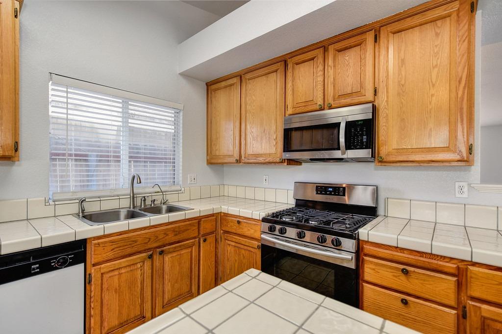 Kitchen with oak cabinets, tiled counters, stainless steel range, and double-basin sink.