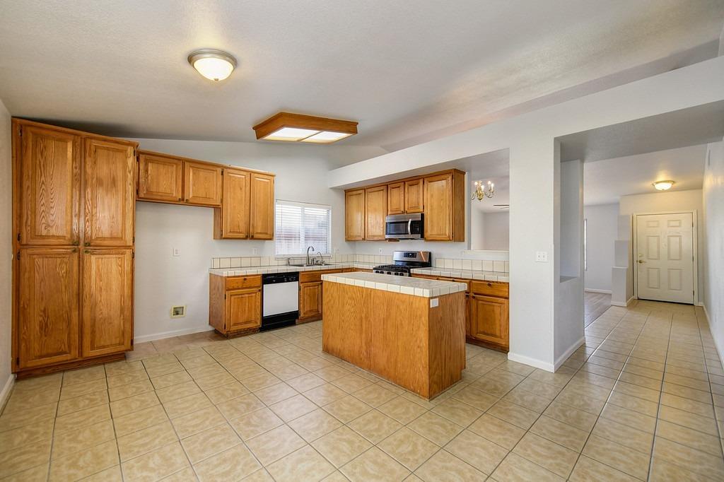 Kitchen with oak cabinets, tiled counters and flooring, center island, and stainless steel appliances.