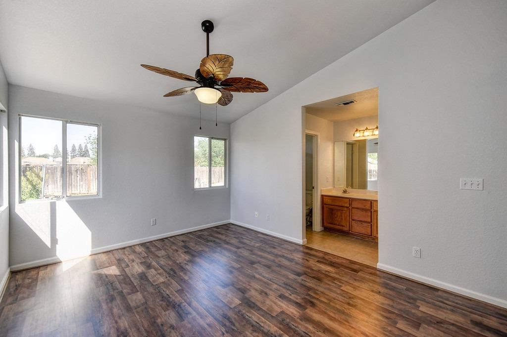 Vacant bedroom with dark wood-look flooring, a leaf-pattern ceiling fan, and an open doorway to the bathroom.