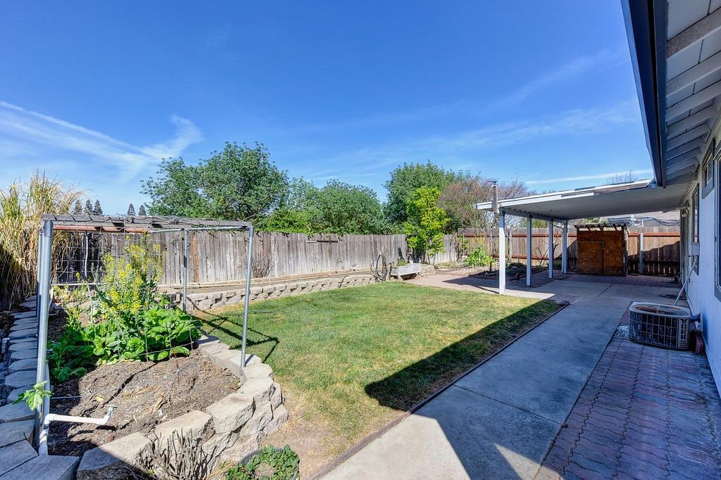 Backyard lawn and stone-edged garden beds beside a covered patio.