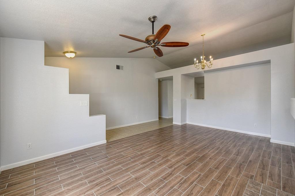 Vacant living and dining area with wood-look tile flooring, ceiling fan, and chandelier.