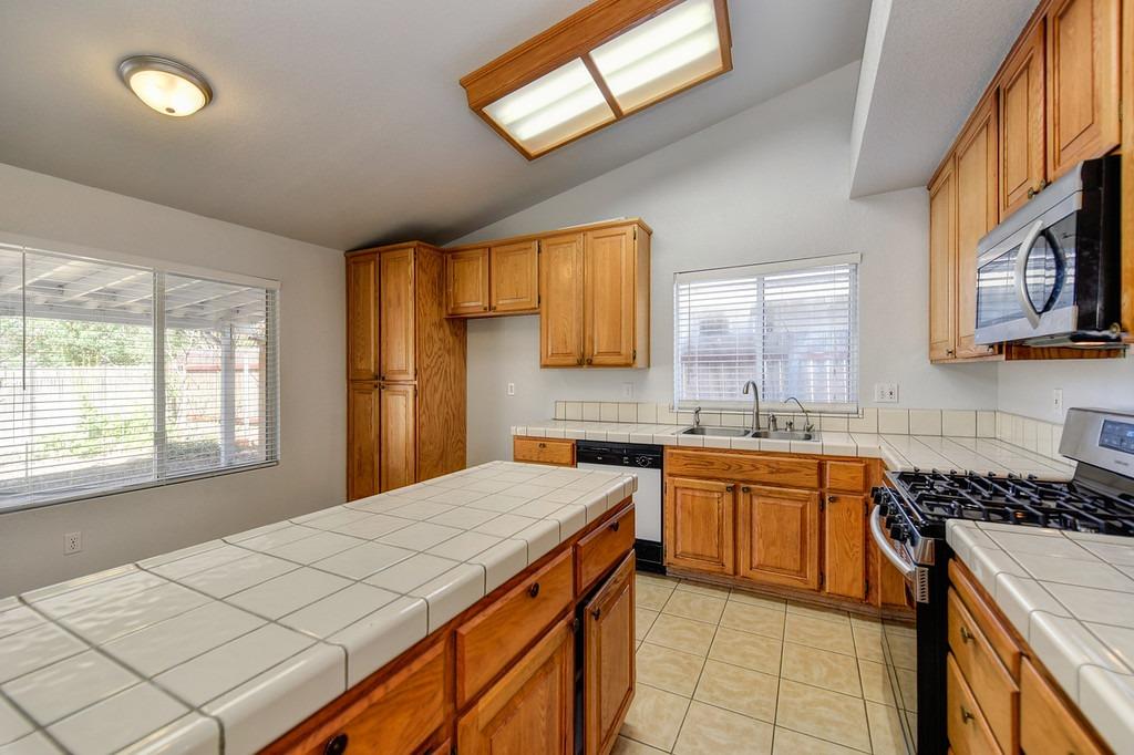 Kitchen with wood cabinets, tiled counters, a large peninsula, and a gas range.