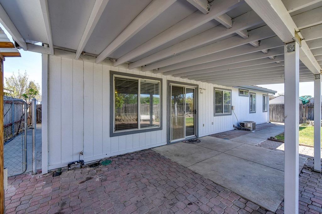 Covered backyard patio with exposed beams, white siding, sliding glass door, and brick-and-concrete flooring.