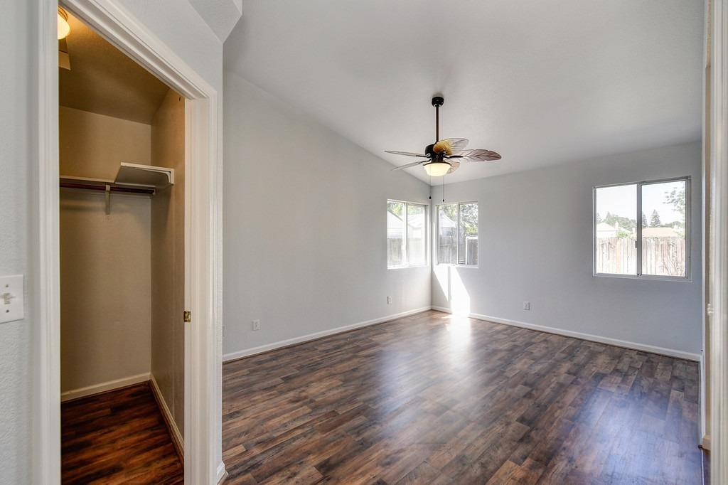 Vacant bedroom with dark wood-look flooring, a ceiling fan, and an open walk-in closet.