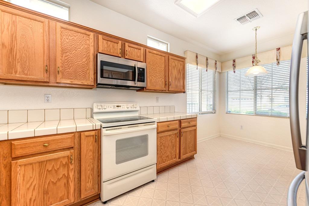 Kitchen with oak cabinets, white tile counters, and large windows with blinds.