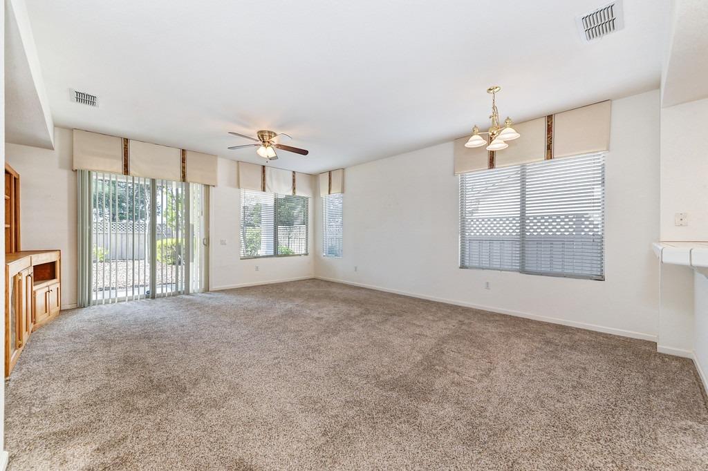 Empty living room with beige carpet, a ceiling fan, and windows overlooking a patio.