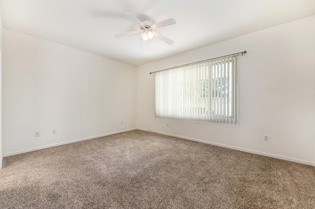 Empty bedroom with beige carpet, a ceiling fan, and a window with vertical blinds.