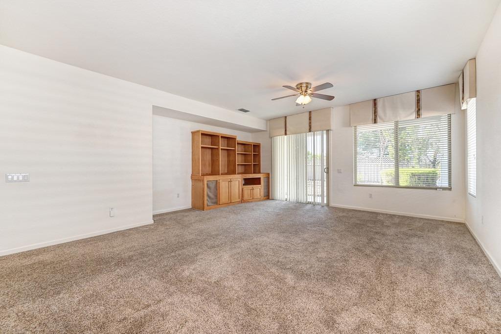 Empty living room with built-in wooden shelving, beige carpet, and large windows.
