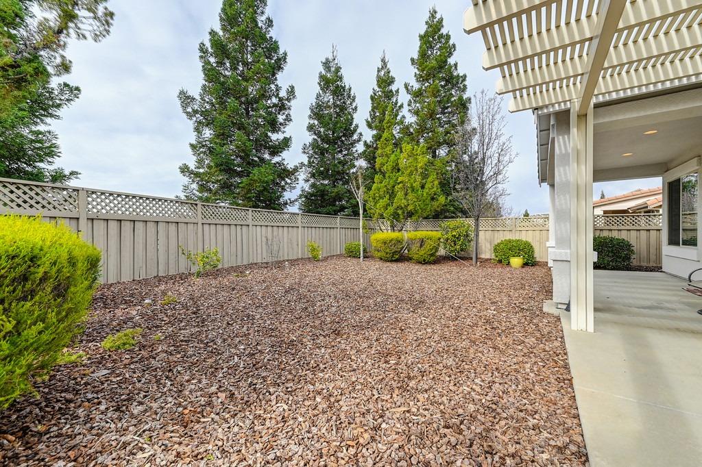 Backyard with wood-chip landscaping, a lattice-topped fence, shrubs, and a covered patio.