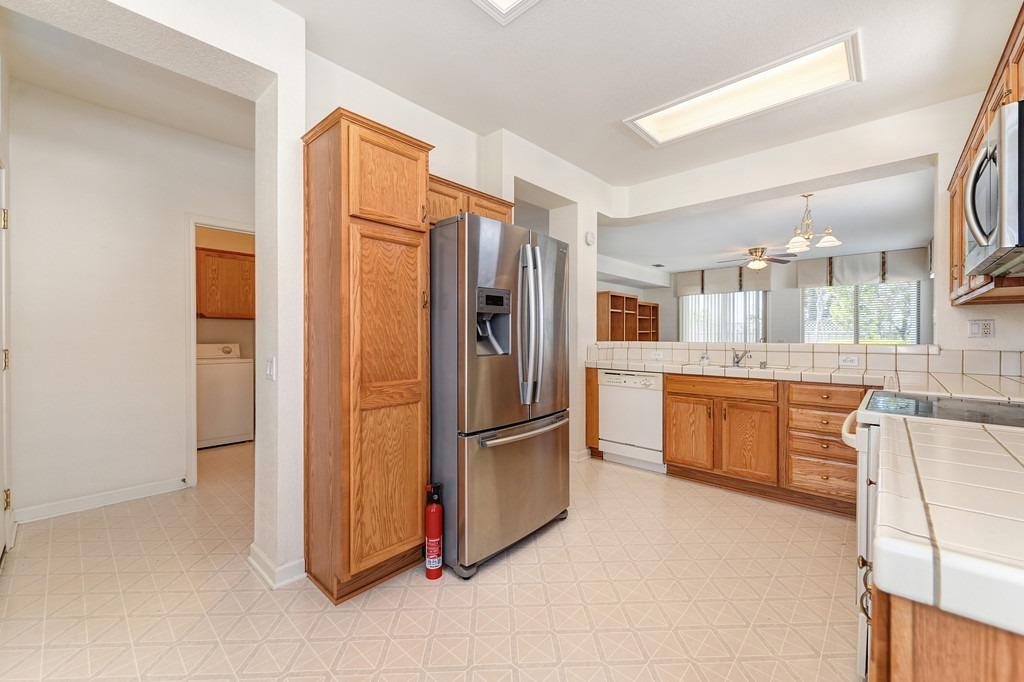 Kitchen with oak cabinets, stainless steel refrigerator, and tiled counters opening to a dining area.
