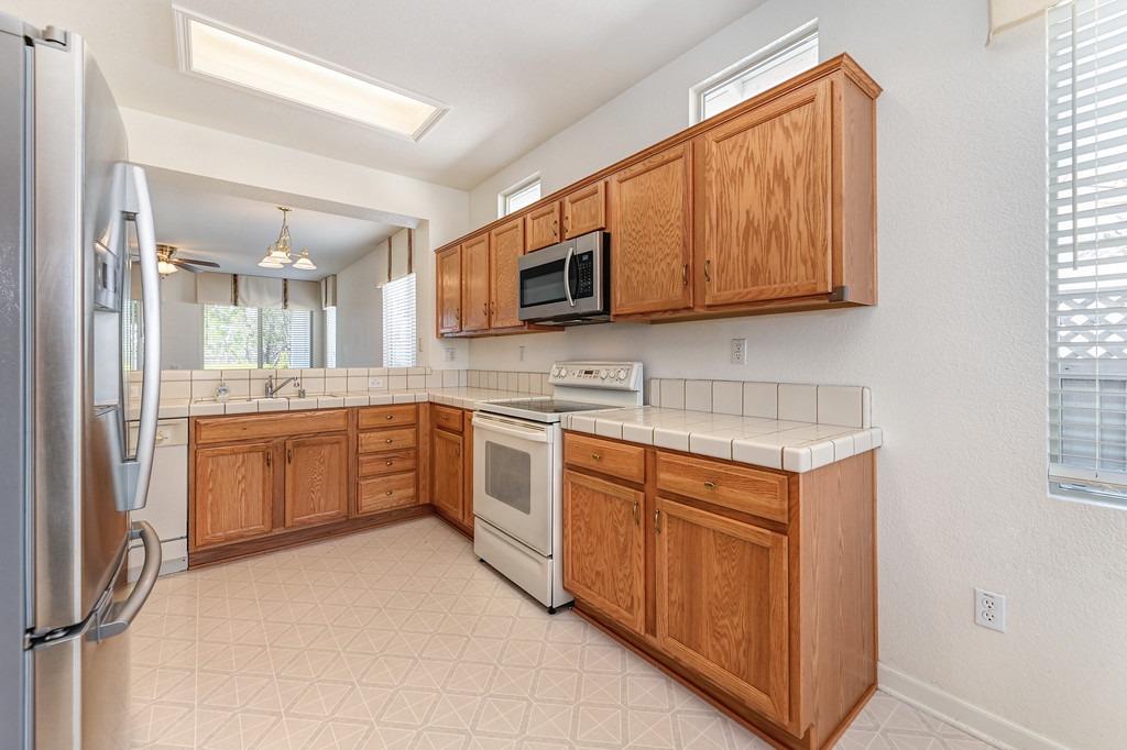 Kitchen with oak cabinets, tiled counters, and stainless steel refrigerator.