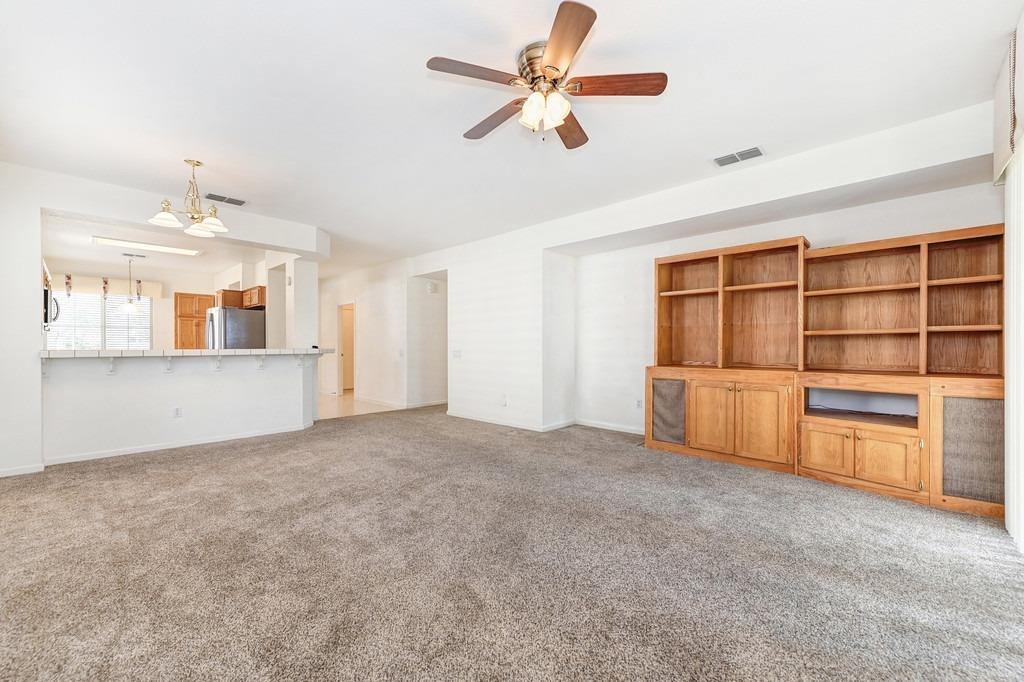 Vacant living room with beige carpet, built-in wood shelving, and an open kitchen beyond.