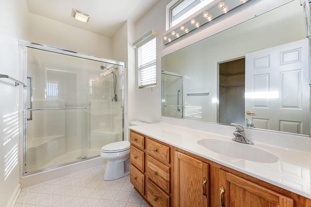 Bathroom with glass-enclosed shower, double-sink vanity, wood cabinets, and a large mirror.