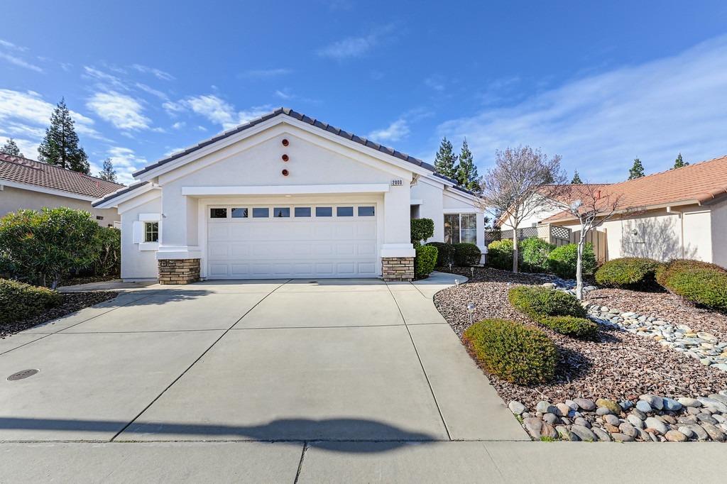 Single-story white house with a wide garage door, broad driveway, and landscaped rock beds.