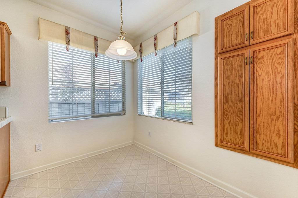 Kitchen area with wood cabinets, two large blinded windows, and patterned tile flooring.