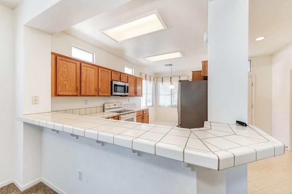Kitchen with wood cabinets, white appliances, and a broad tiled peninsula counter.