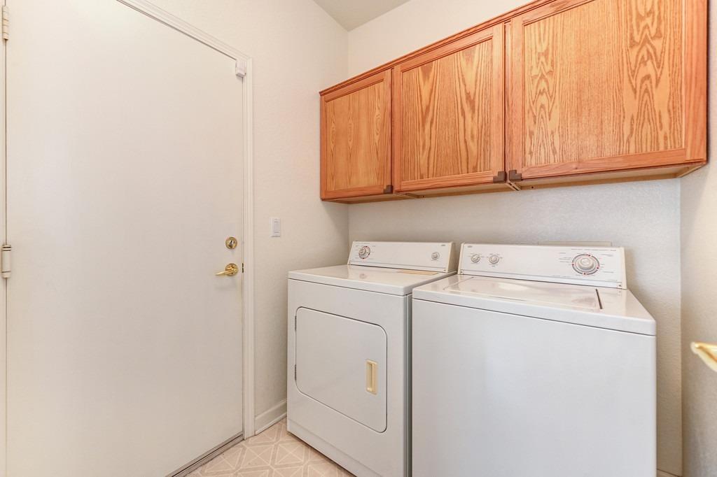 Laundry room with white washer and dryer beneath oak cabinets.