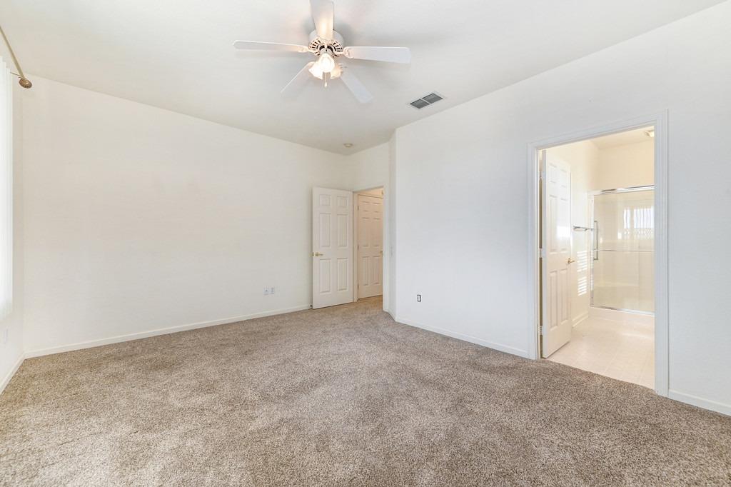 Empty carpeted bedroom with a ceiling fan and an open doorway to an ensuite bathroom.