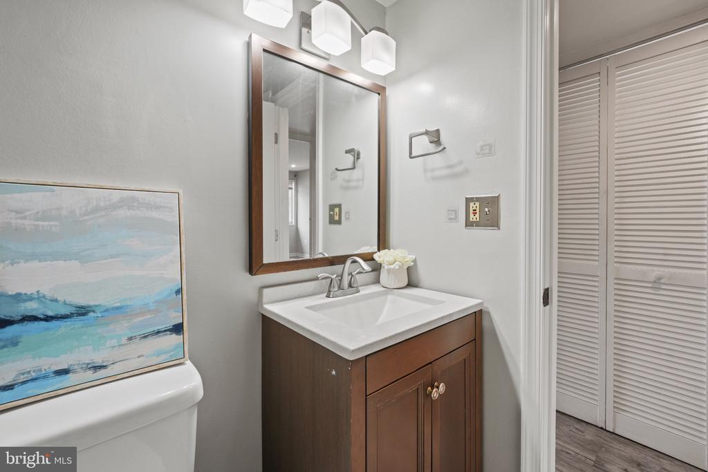 Bathroom vanity with dark wood cabinet, white countertop, framed mirror, and louvered closet doors.