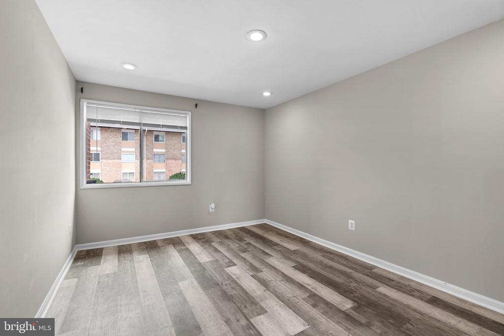 Empty bedroom with recessed lights, window blinds, and mixed-tone plank flooring.
