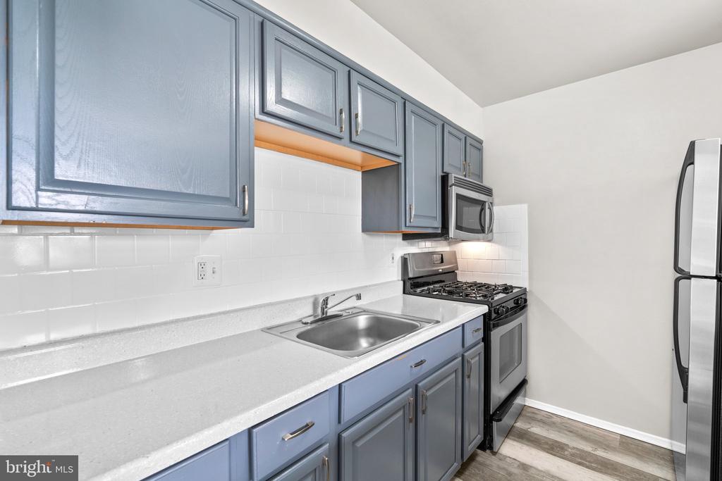 Kitchen with blue-gray cabinets, white counters, subway tile backsplash, and stainless steel appliances.