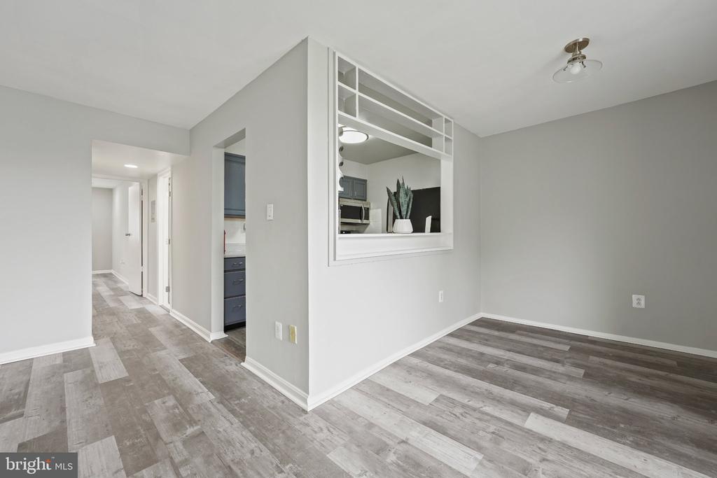 Empty dining area with gray plank flooring and a wide pass-through to the kitchen.
