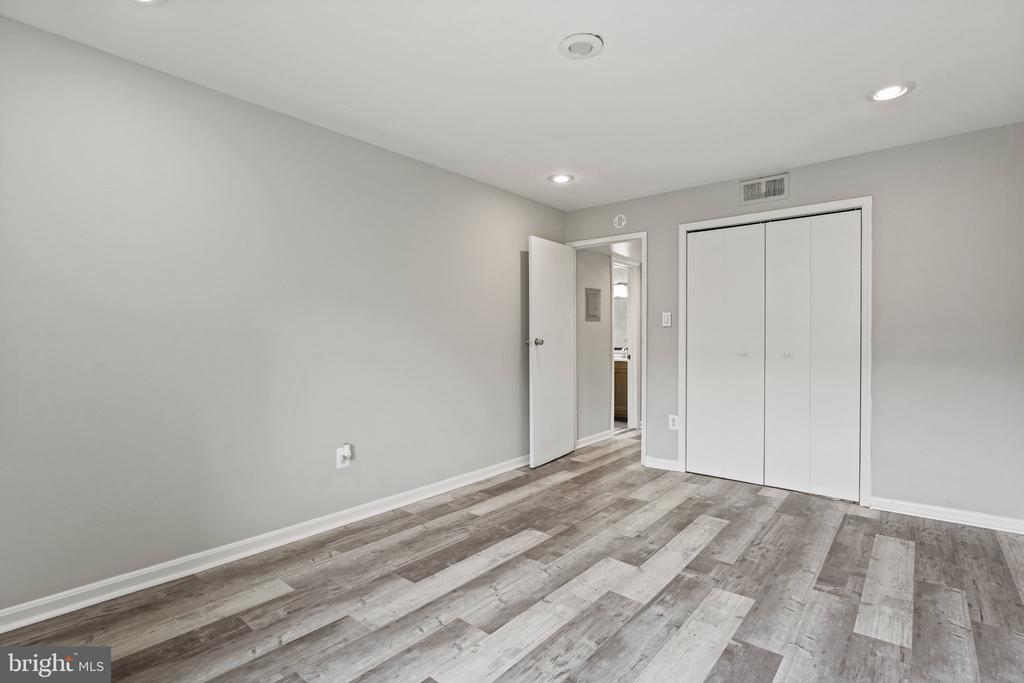 Empty bedroom with gray-and-white plank flooring, a white closet, and an open doorway.