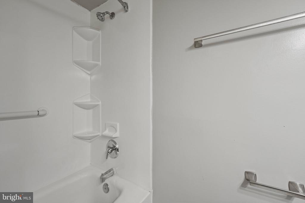 White bathtub and shower alcove with built-in corner shelves and chrome fixtures.