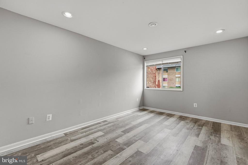 Empty room with gray walls, recessed lights, and wood-look flooring beside a window.