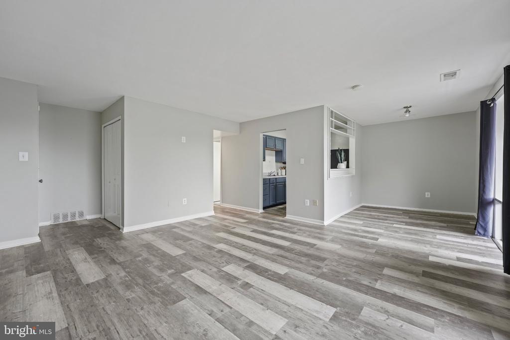 Unfurnished living room with gray plank flooring, a pass-through to the kitchen, and sliding glass doors.