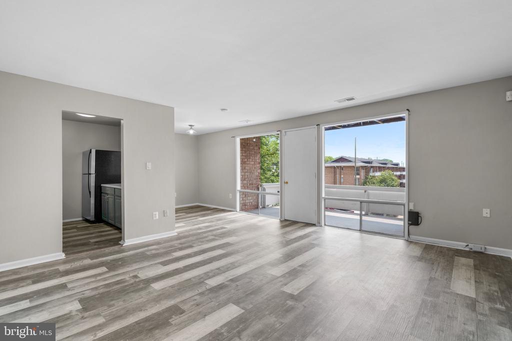 Vacant living room with plank flooring, a kitchen opening, and sliding glass doors to a balcony.