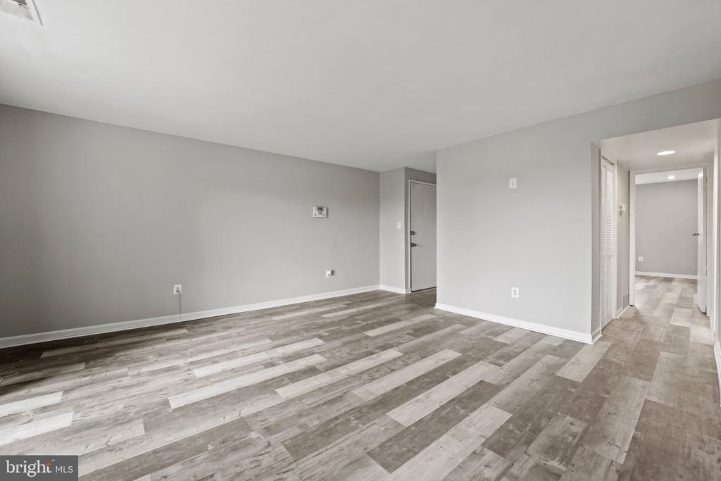 Vacant living room with gray-toned plank flooring and a hallway leading to adjoining rooms.