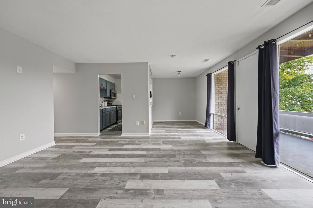 Vacant living area with gray plank flooring, a kitchen doorway, and sliding glass doors to a balcony.