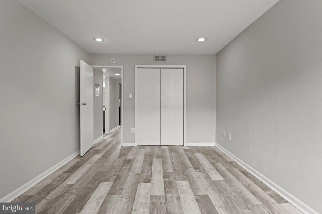 Empty room with a double-door closet, recessed lights, and gray wood-look flooring.
