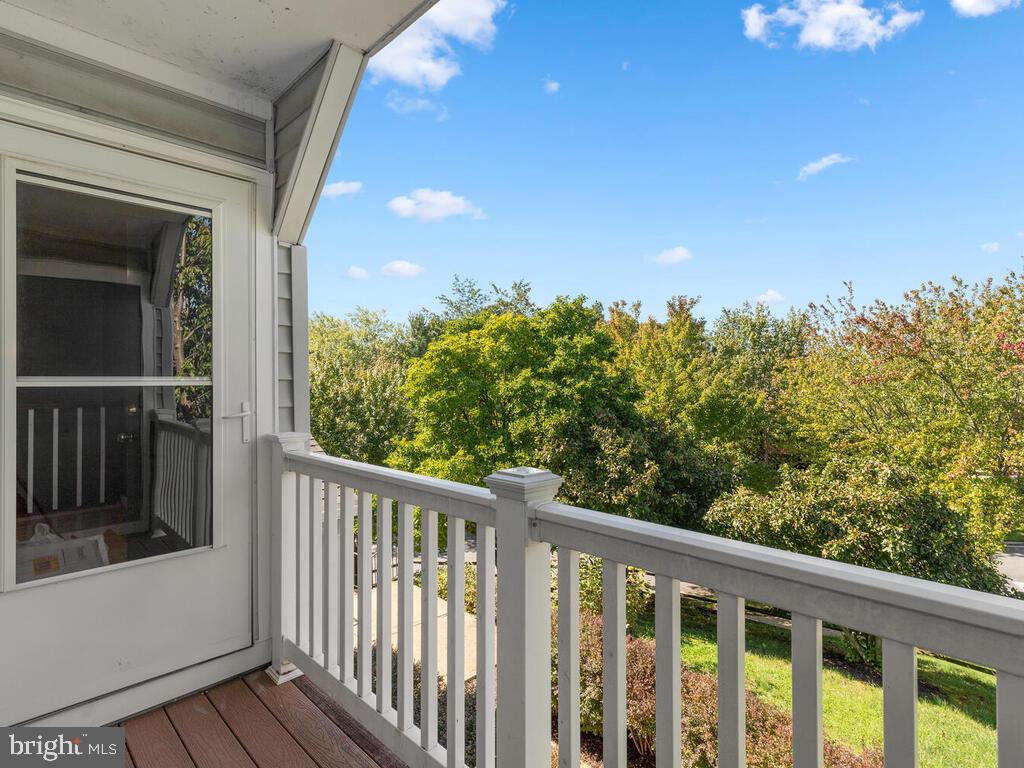 Covered porch with white railing overlooking leafy trees and a sunny yard.