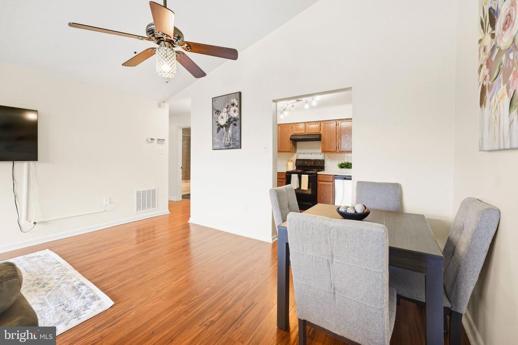 Dining and living area with hardwood floors, gray chairs, and an adjoining wood-cabinet kitchen.