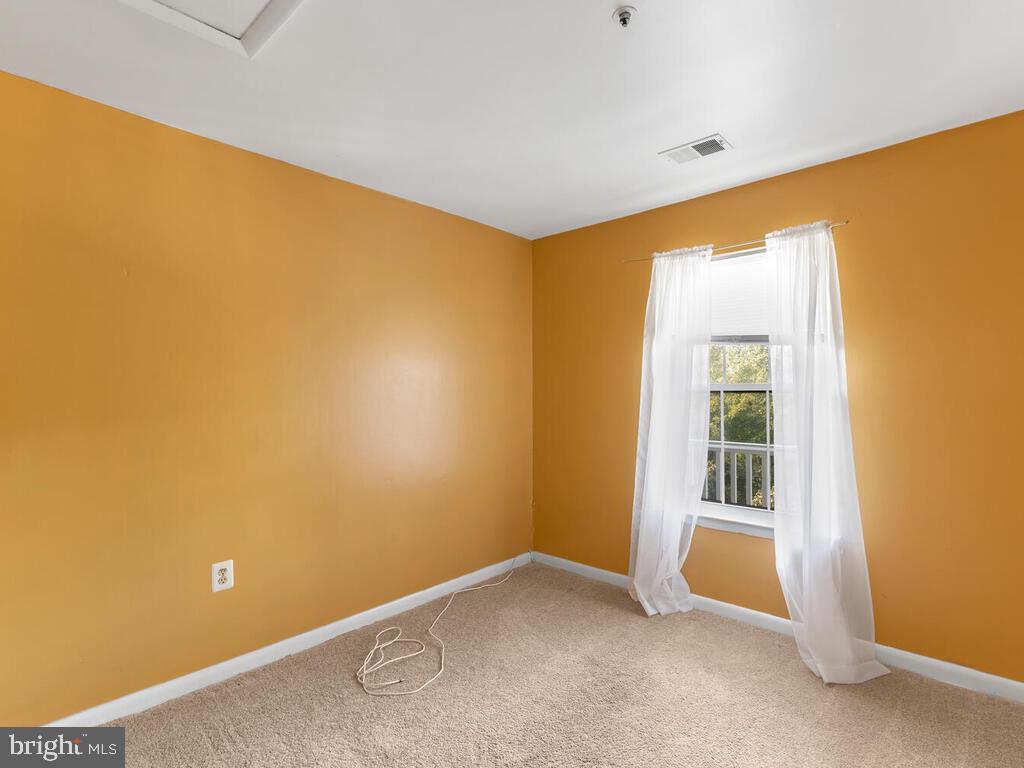 Empty bedroom with orange walls, beige carpet, and a curtained window overlooking trees.