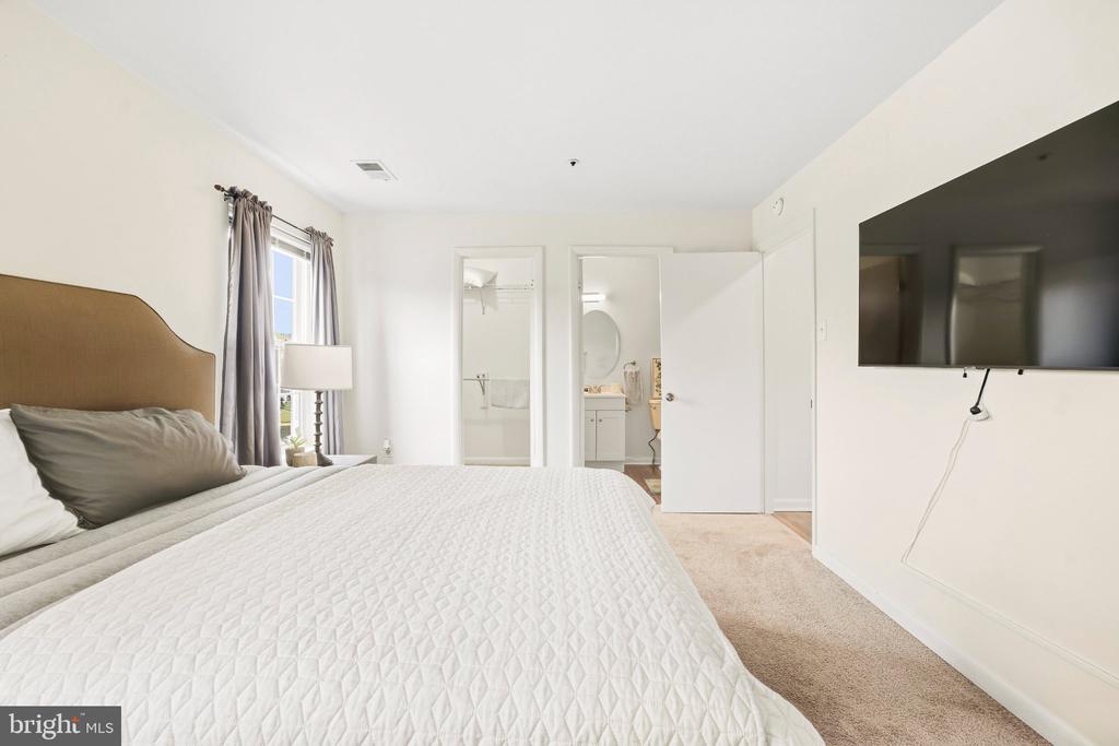 Bedroom with a quilted white bedspread, gray curtains, and a wall-mounted television.