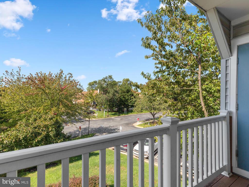 Balcony overlooking a leafy residential street, with a white railing and blue door.