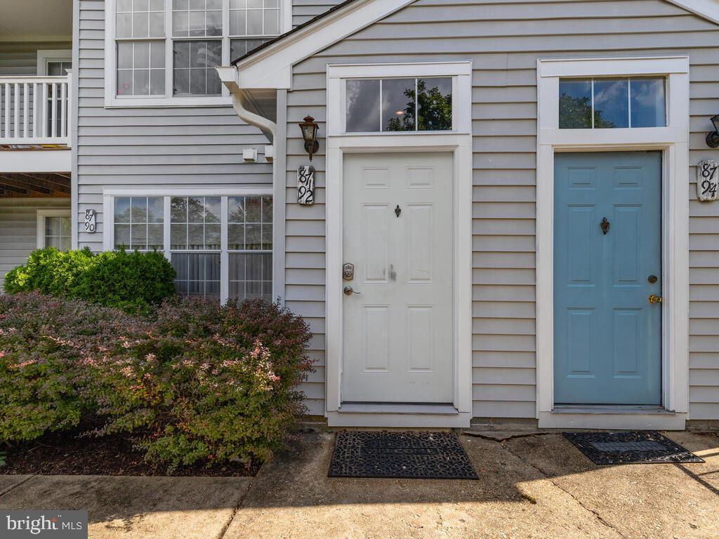 Attached home exterior with a white front door, blue neighboring door, and shrubs along the facade.