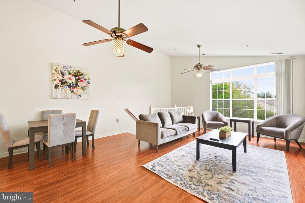 Open-plan living and dining room with reddish hardwood floors, ceiling fans, and a large window.