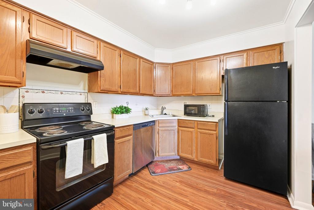 Kitchen with honey-toned wood cabinets, black appliances, white countertops, and wood-look flooring.