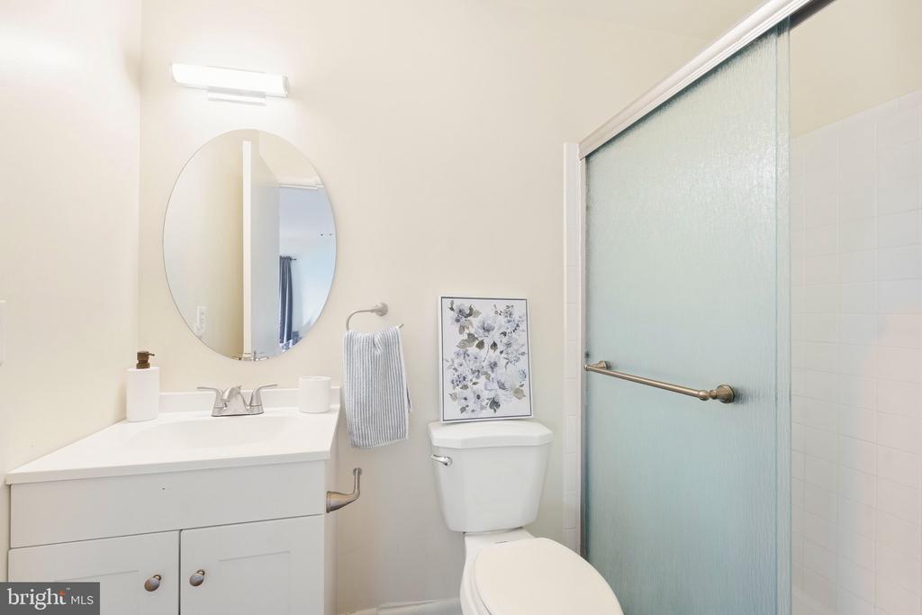 Bathroom with a white vanity, oval mirror, floral artwork above the toilet, and frosted-glass shower.
